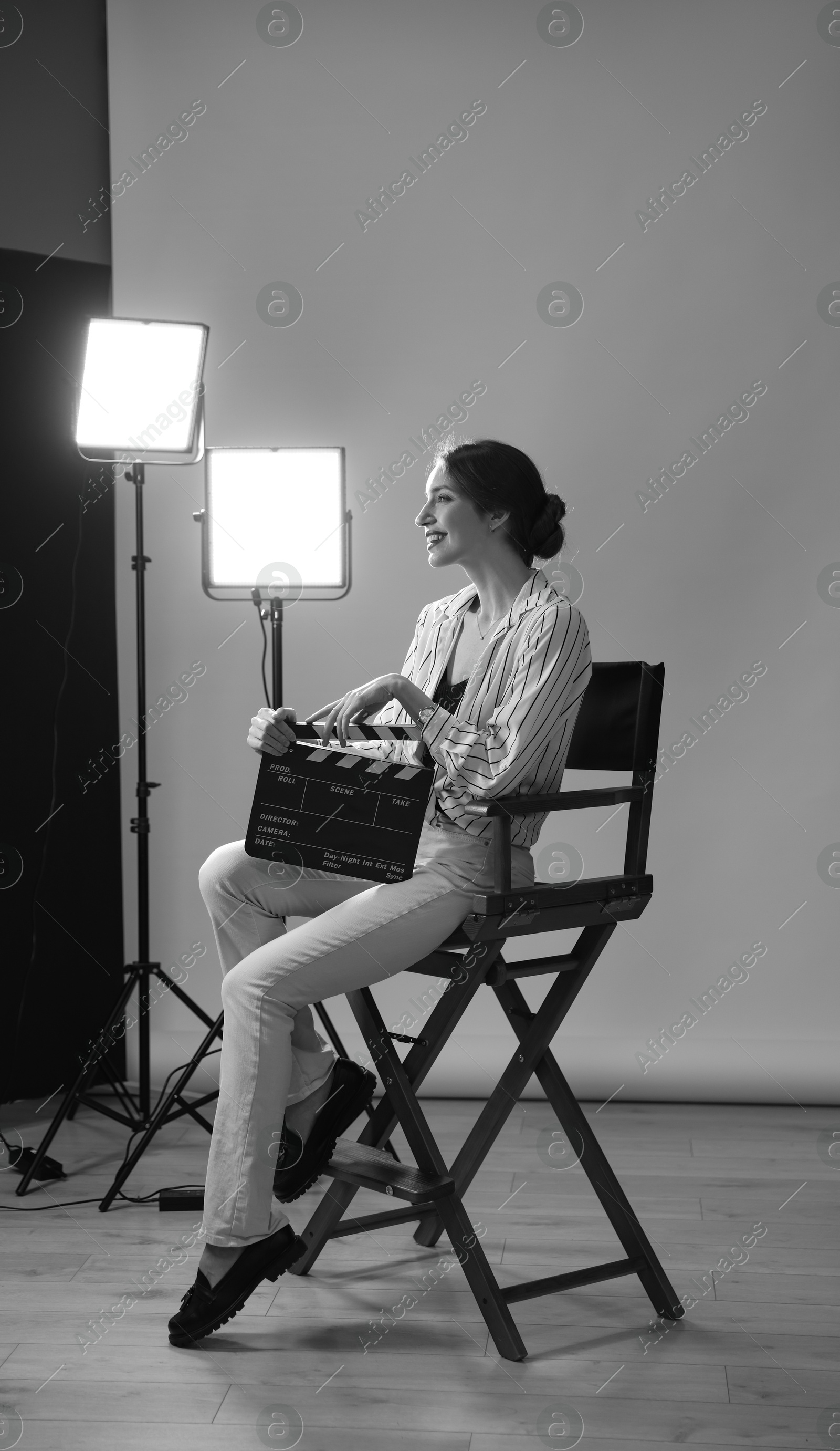 Photo of Beautiful woman with clapperboard sitting in director's chair in studio. Black and white effect