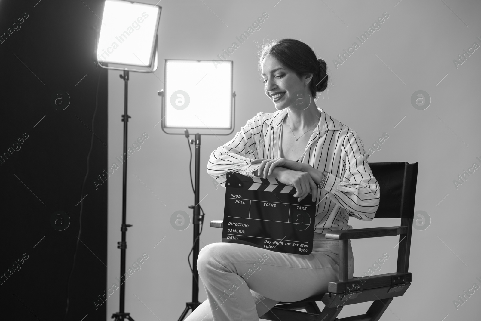 Photo of Beautiful woman with clapperboard sitting in director's chair in studio. Black and white effect