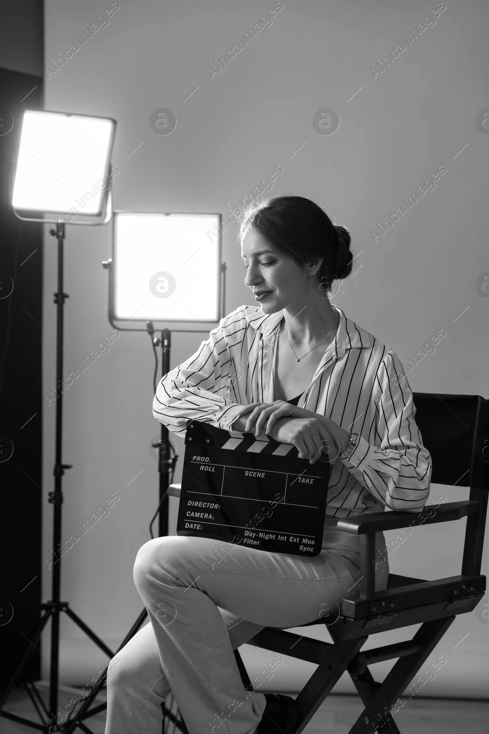 Photo of Beautiful woman with clapperboard sitting in director's chair in studio. Black and white effect