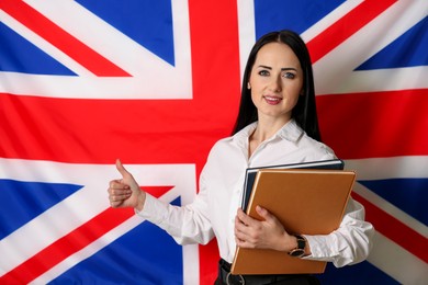 English teacher with books showing thumbs up against UK flag