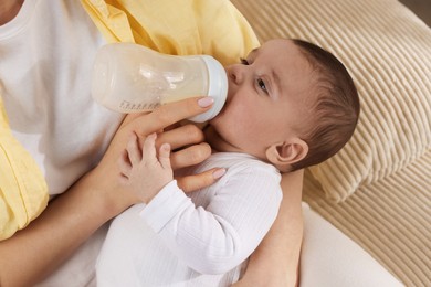 Photo of Mother feeding her little baby from bottle indoors, closeup