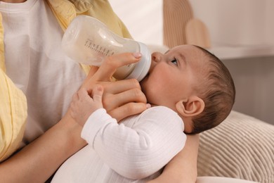 Photo of Mother feeding her little baby from bottle indoors, closeup