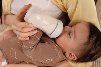 Photo of Mother feeding her little baby from bottle indoors, closeup