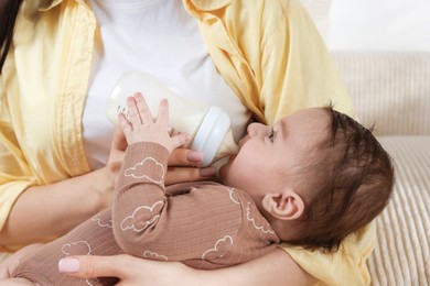 Photo of Mother feeding her little baby from bottle indoors, closeup