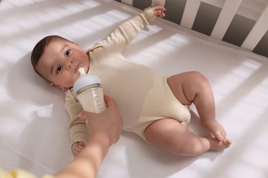 Mother feeding her little baby from bottle indoors, top view