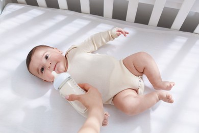 Photo of Mother feeding her little baby from bottle indoors, top view