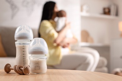 Mother holding her little baby indoors, focus on feeding bottles with milk and teether