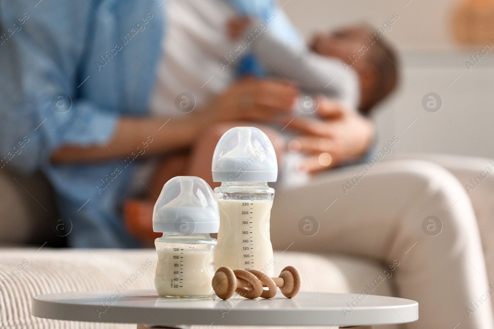 Photo of Mother holding her little baby indoors, focus on feeding bottles with milk and teether