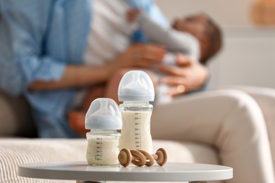 Mother holding her little baby indoors, focus on feeding bottles with milk and teether