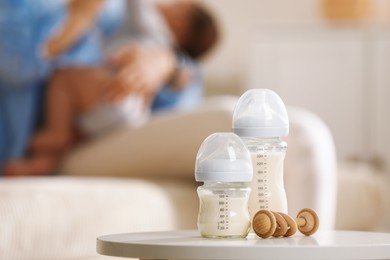 Photo of Mother holding her little baby indoors, focus on feeding bottles with milk and teether