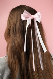 Woman with stylish hair bow on pink background, back view