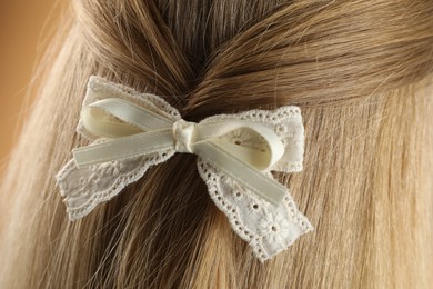 Photo of Woman with beautiful hair bow on beige background, closeup