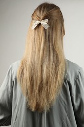 Woman with beautiful hair bow on light grey background, back view