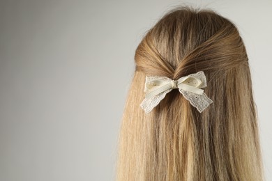 Photo of Woman with beautiful hair bow on light grey background, back view. Space for text