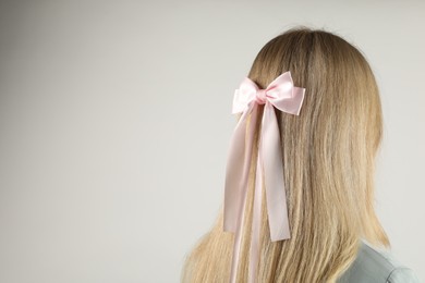 Photo of Woman with beautiful hair bow on light grey background, back view. Space for text