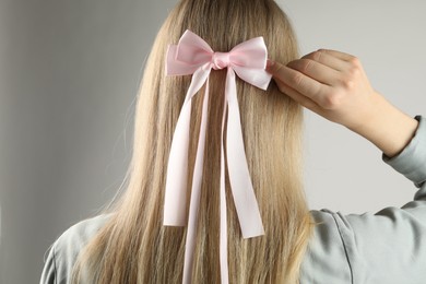 Woman with beautiful hair bow on light grey background, back view