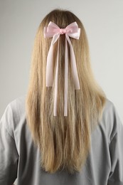 Woman with beautiful hair bow on light grey background, back view