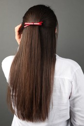 Woman with beautiful hair clip on grey background, back view