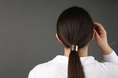 Woman with beautiful hair tie on grey background, back view. Space for text