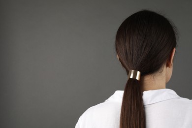 Woman with beautiful hair tie on grey background, back view. Space for text