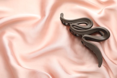 Photo of Beautiful hair clip on pink silk fabric, above view. Space for text