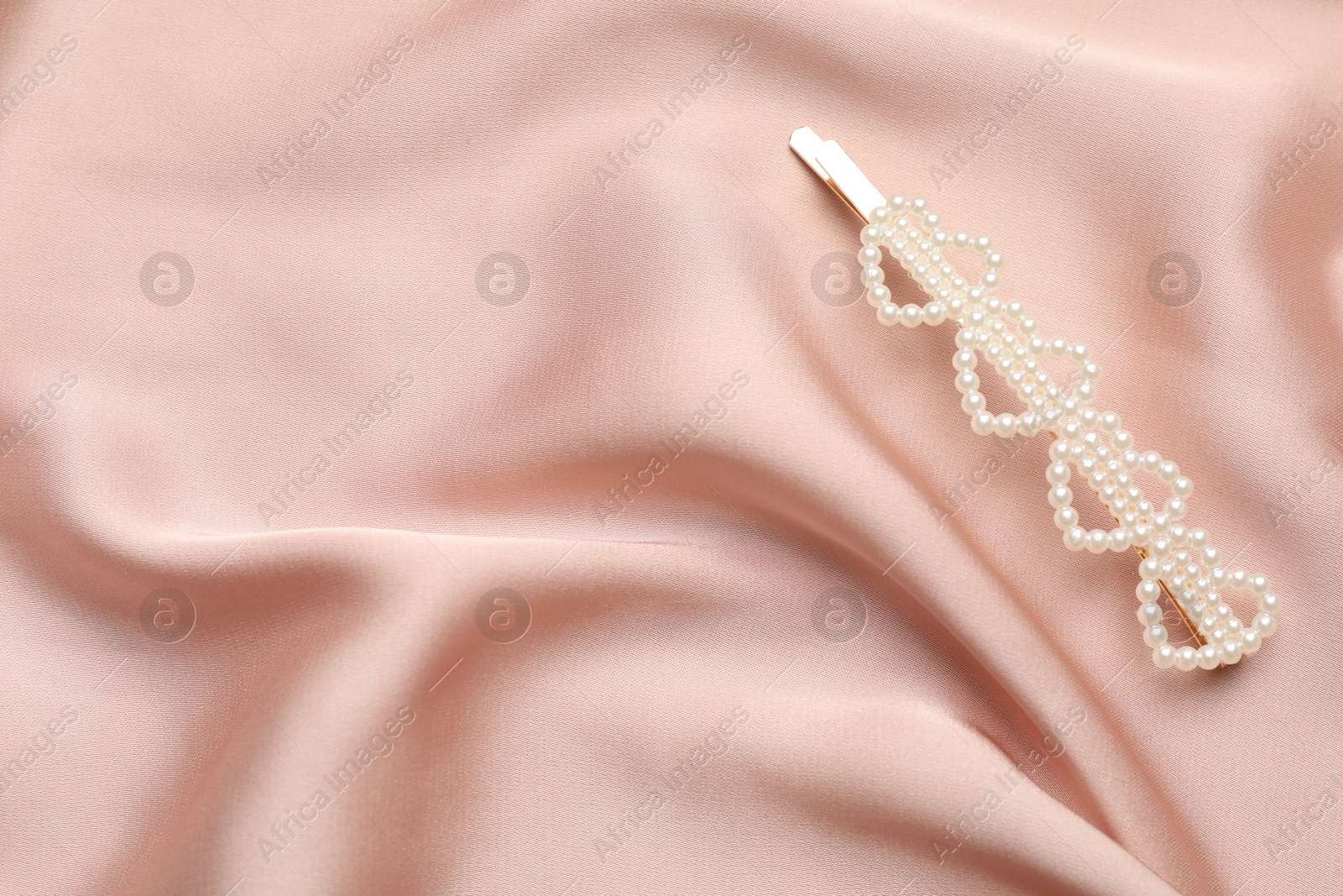 Photo of Beautiful hair clip on pink silk fabric, above view. Space for text