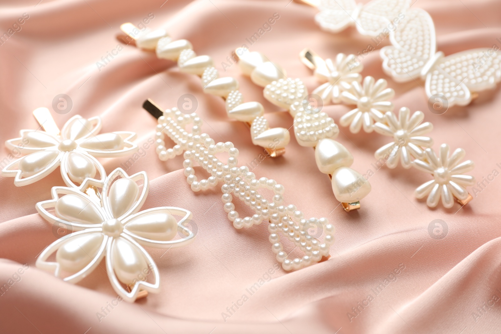 Photo of Beautiful hair clips on pink silk fabric, closeup