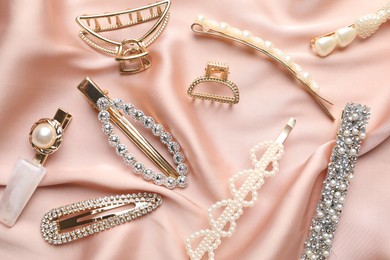 Photo of Beautiful hair accessories on pink silk fabric, flat lay