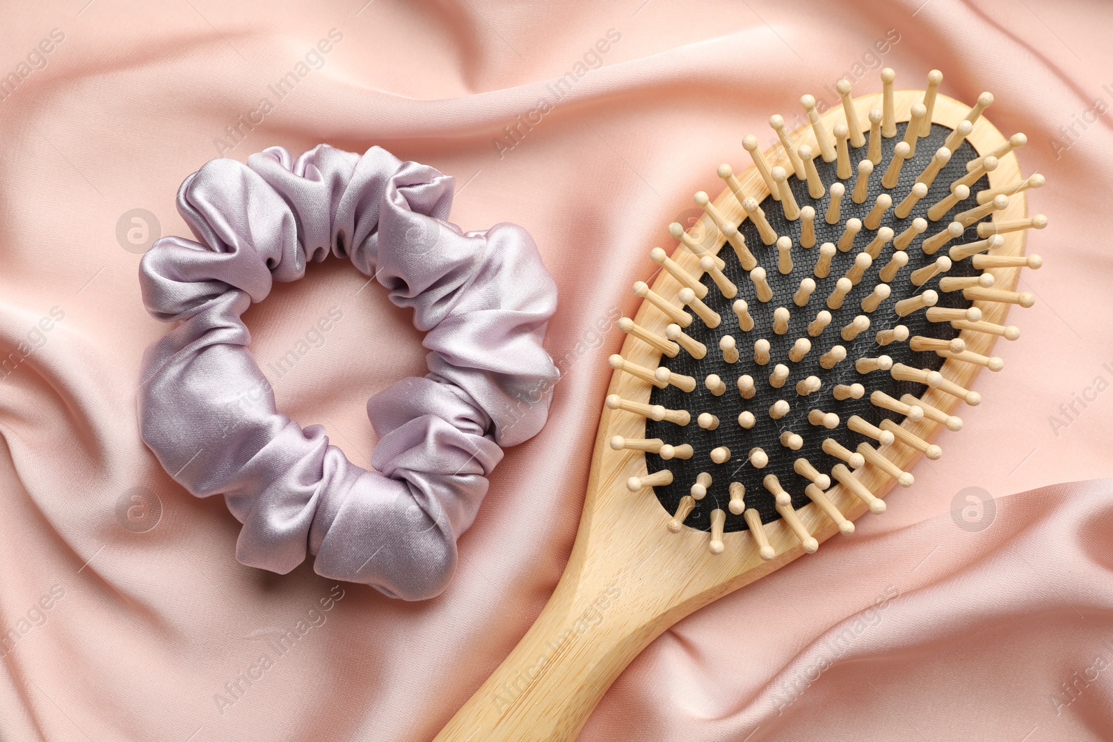 Photo of Hair scrunchie and brush on pink silk fabric, flat lay