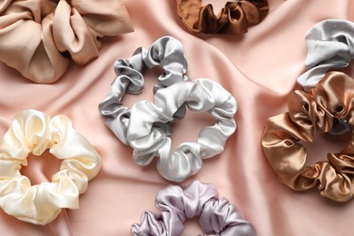 Photo of Different hair scrunchies on pink silk fabric, flat lay