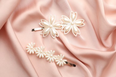 Photo of Beautiful hair clips on pink silk fabric, flat lay