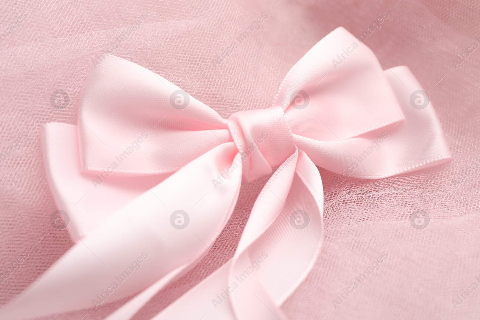 Photo of Beautiful hair bow on pink tulle fabric, closeup