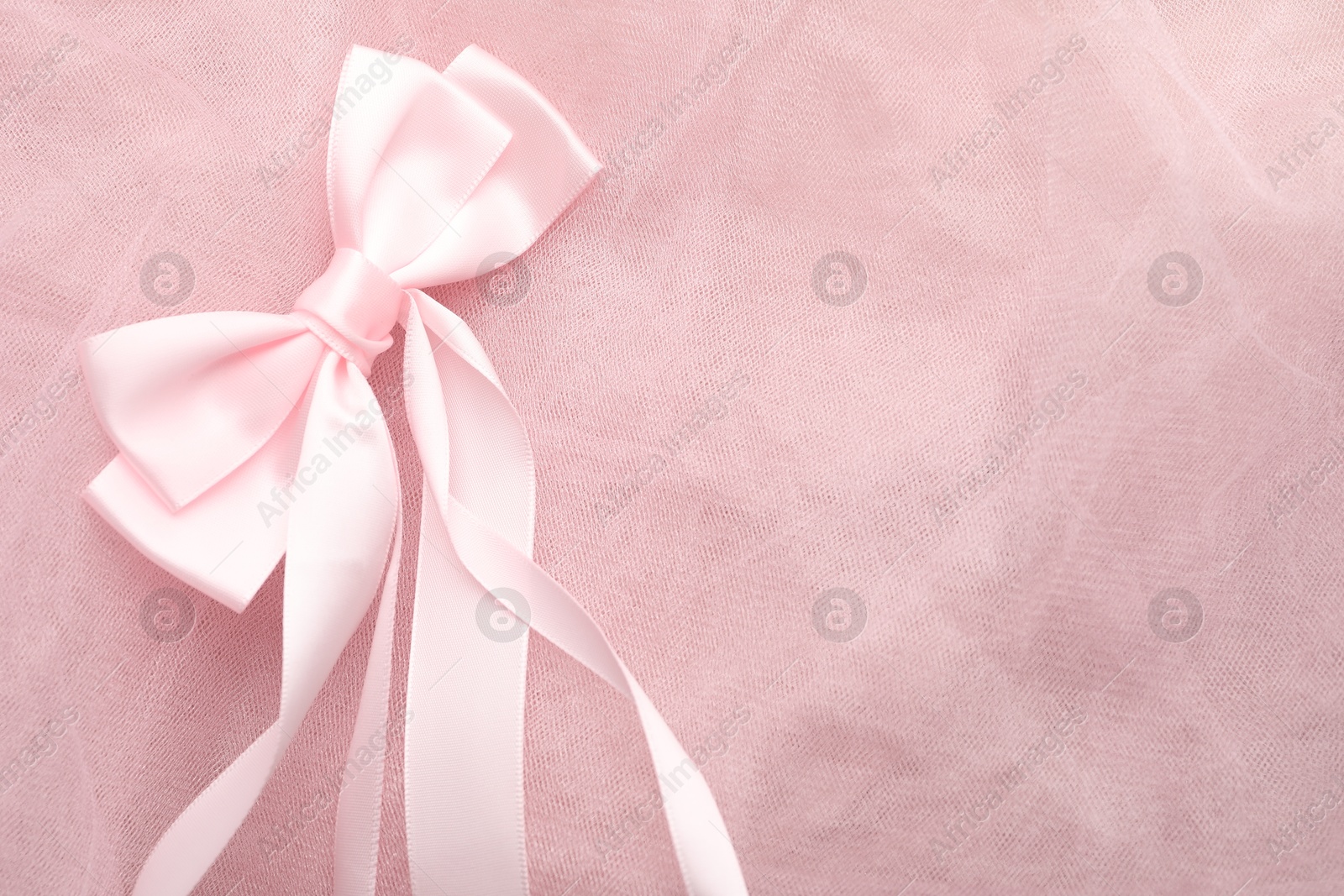 Photo of Beautiful hair bow on pink tulle fabric, top view. Space for text