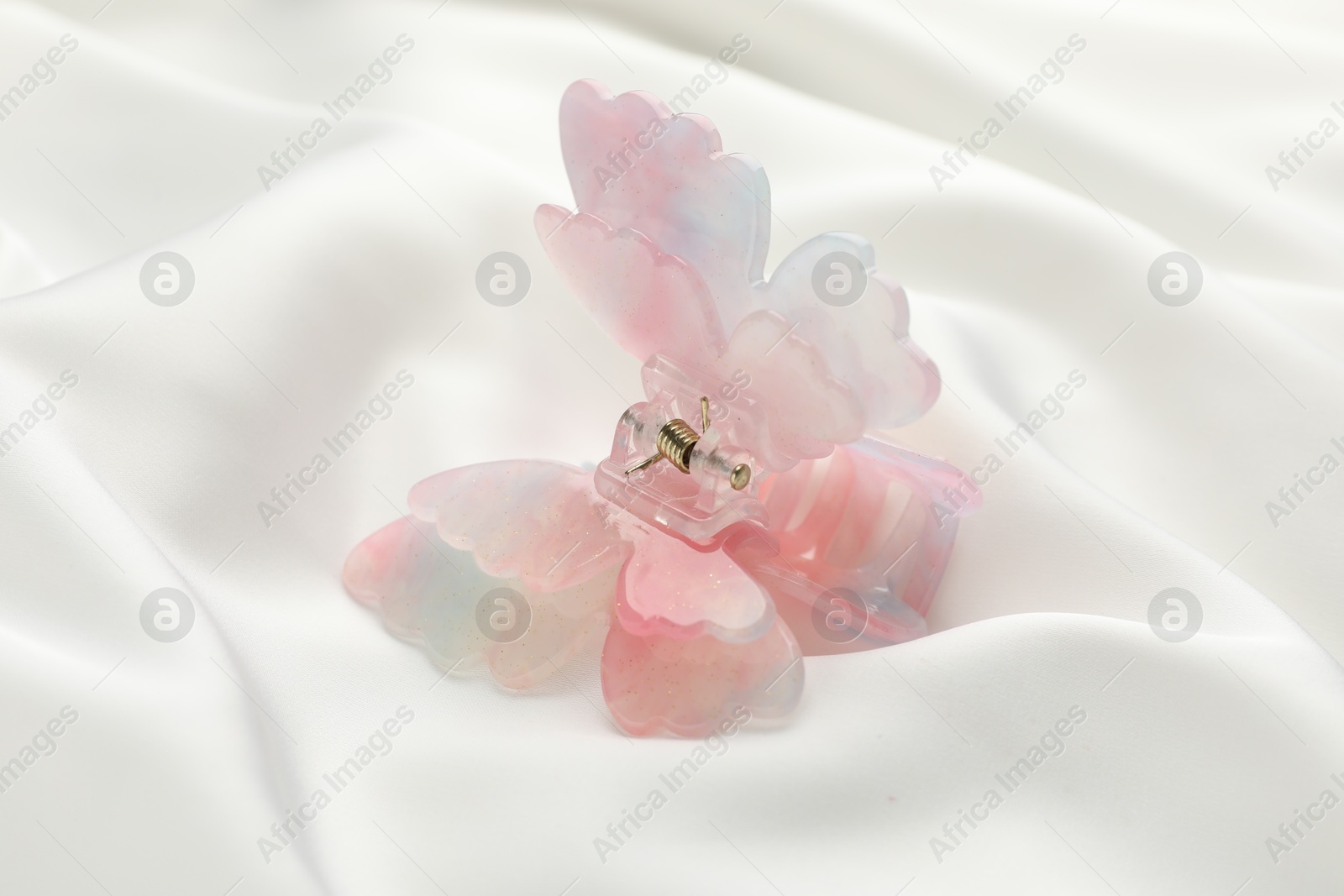 Photo of Beautiful hair clip on white silk fabric, closeup