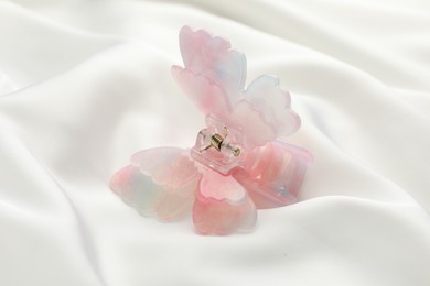 Photo of Beautiful hair clip on white silk fabric, closeup