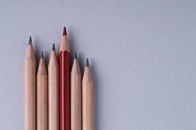 One red pencil among graphite ones on light grey background, top view. Space for text