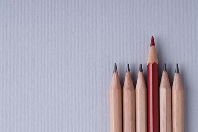 One red pencil among graphite ones on light grey background, top view. Space for text