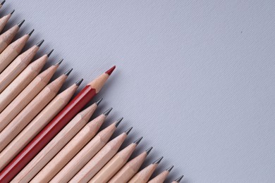 One red pencil among graphite ones on light grey background, top view. Space for text