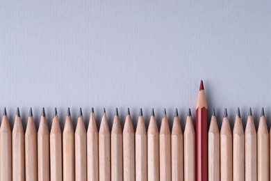 One red pencil among graphite ones on light grey background, top view. Space for text