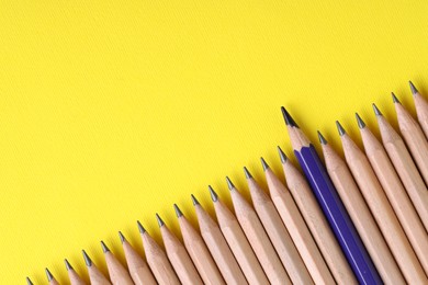 Photo of One blue pencil among graphite ones on yellow background, top view. Space for text