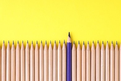 Photo of One blue pencil among graphite ones on yellow background, top view. Space for text