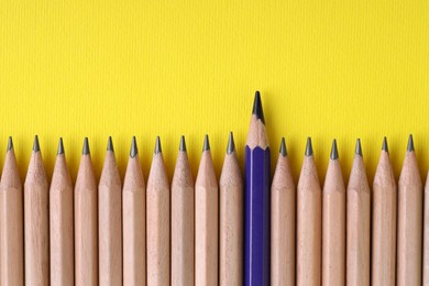 Photo of One blue pencil among graphite ones on yellow background, top view. Space for text