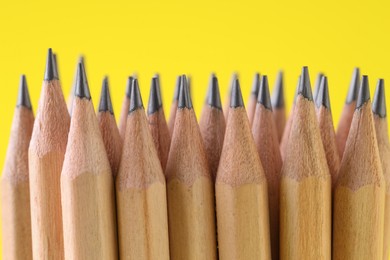 Photo of Many graphite pencils on yellow background, closeup