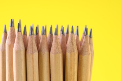 Photo of Many graphite pencils on yellow background, closeup