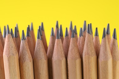 Photo of Many graphite pencils on yellow background, closeup