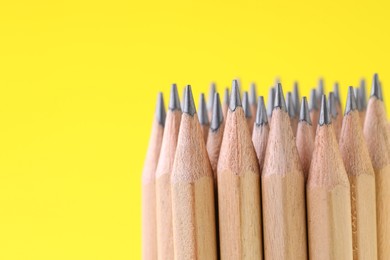 Photo of Many graphite pencils on yellow background, closeup. Space for text