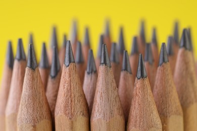 Photo of Many graphite pencils on yellow background, closeup