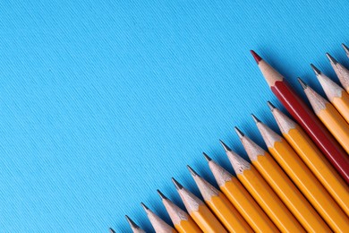 Photo of One red pencil among graphite ones on light blue background, top view. Space for text