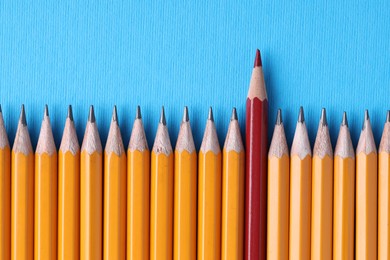 Photo of One red pencil among graphite ones on light blue background, top view