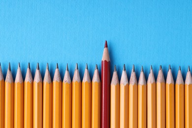 Photo of One red pencil among graphite ones on light blue background, top view. Space for text